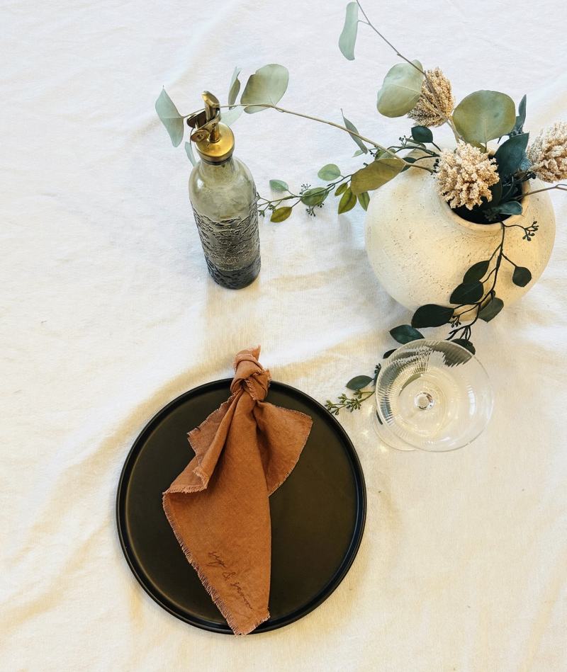 Terracotta linen napkin embroidered sip and savor on a black plate