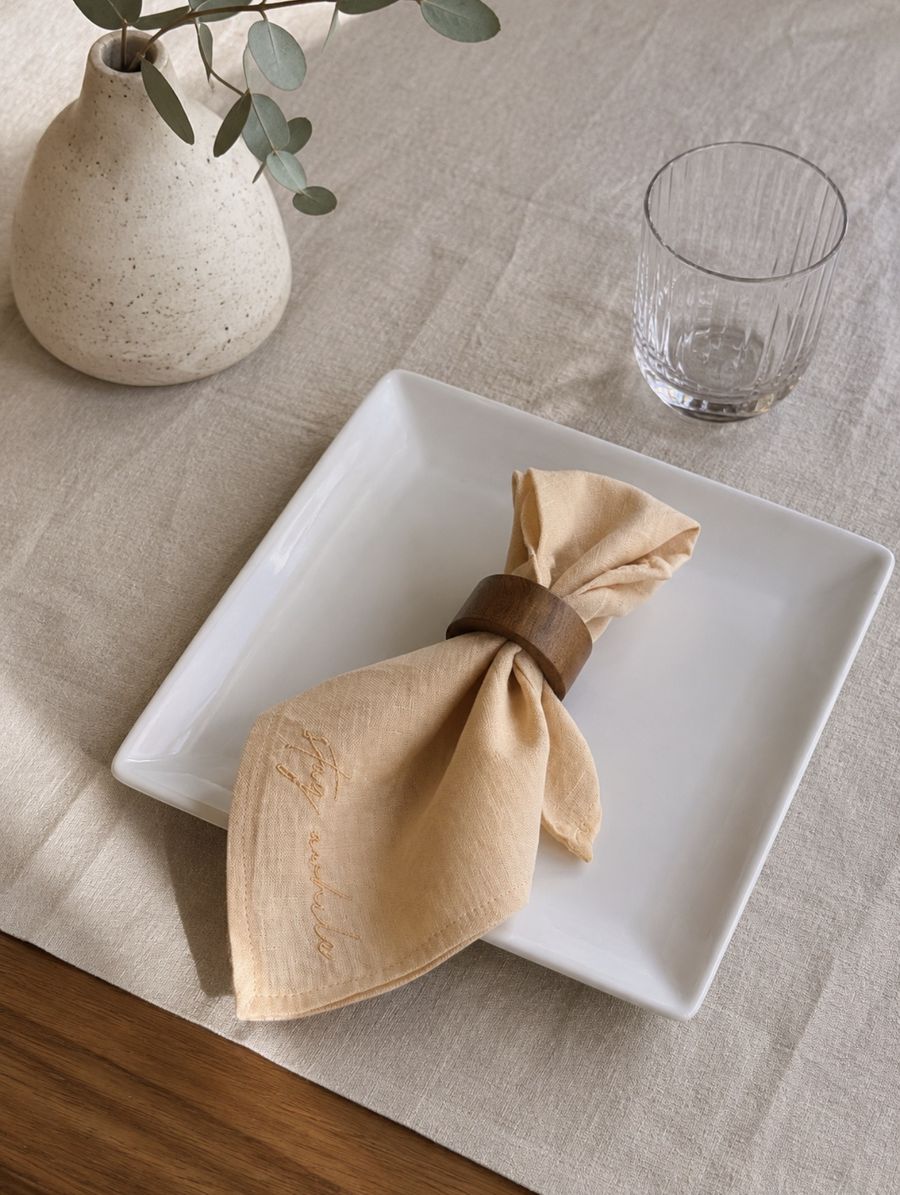 Stay a while embroidered linen napkin folded on a plate with a wooden napkin ring