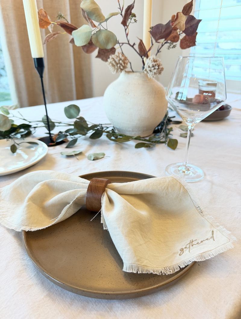 Gathered embroidered linen napkin in a wooden napkin ring at a full table setting