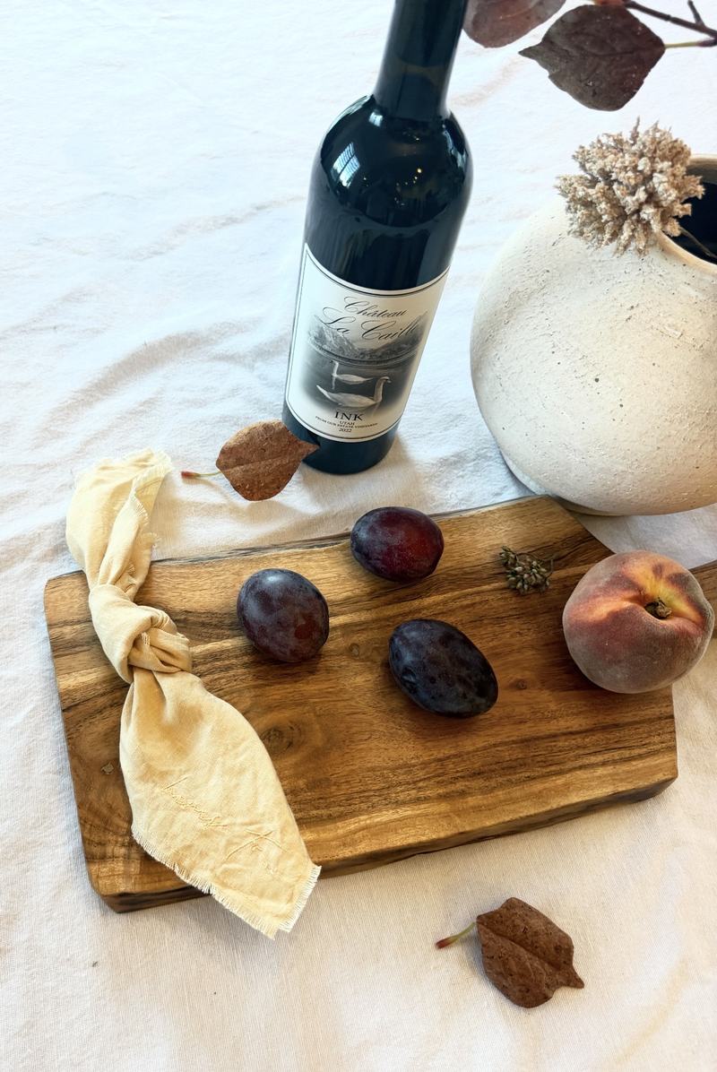 Wine, plums, and a peach on a wooden board with a linen napkin